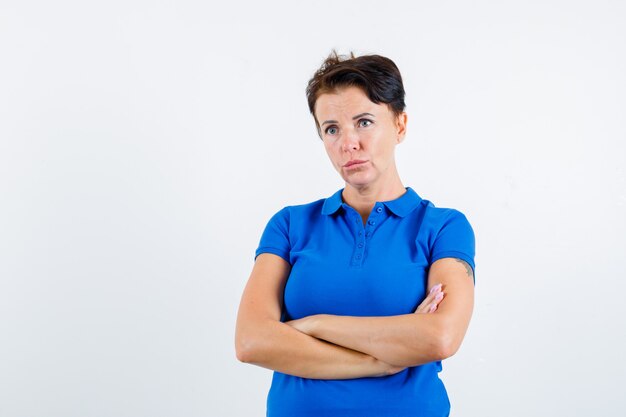 Portrait of mature woman standing with crossed arms in blue t-shirt and looking pensive front view