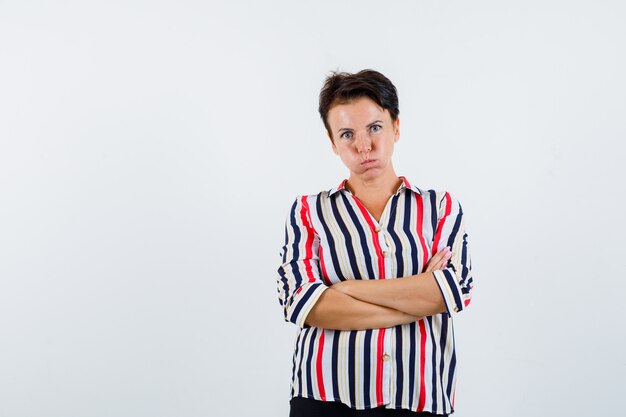 Portrait of mature woman standing with crossed arms in striped shirt and looking bored front view