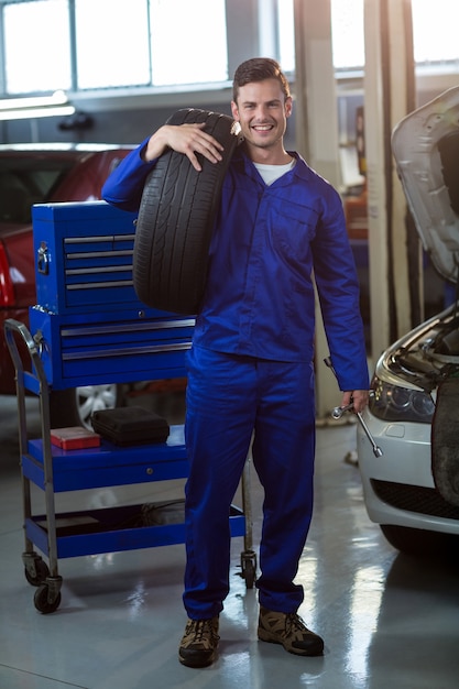 Free photo portrait of mechanic carrying a tyre