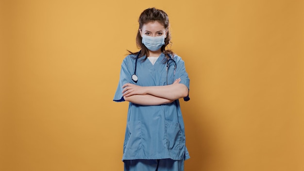 Portrait of medic wearing corona virus protection and hospital uniform looking professional in studio. Woman doctor with arms crossed posing confident wearing covid protection and stethoscope.