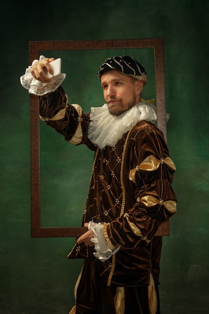 Portrait of medieval young man in vintage clothing with wooden frame on dark wall