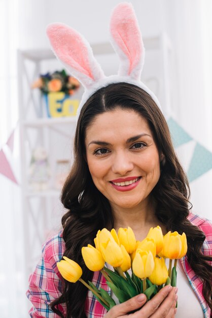 Portrait of a mid adult woman with bunny ear's on her head holding yellow tulips in hand looking to camera