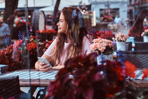 Portrait of a middle age businesswoman with long brown hair holds a smartphone while sitting at an outdoor cafe.