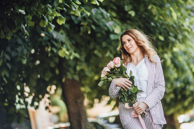 Portrait of a middle-aged blonde woman in casual clothes in the street with a bouquet of roses