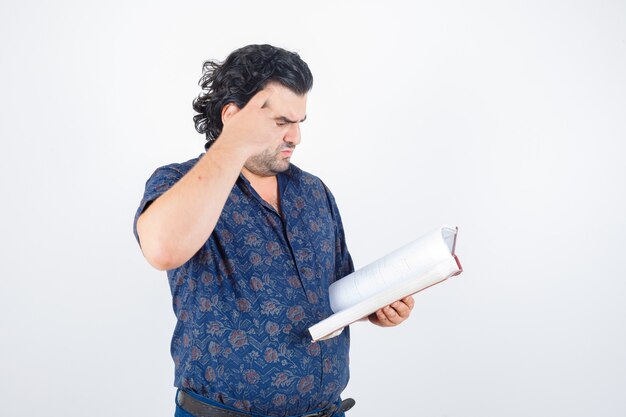 Portrait of middle aged man looking through book in shirt and looking thoughtful front view