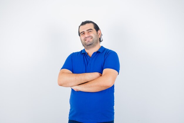 Portrait of middle aged man standing with crossed arms in blue t-shirt and looking happy