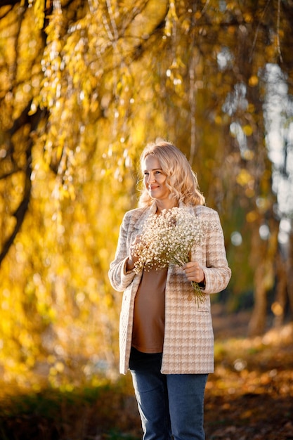 Портрет беременной женщины средних лет на открытом воздухе в парке Беременная женщина среднего возраста, ожидающая ребенка в возрасте беременности Блондинка в коричневом свитере и бежевом пальто