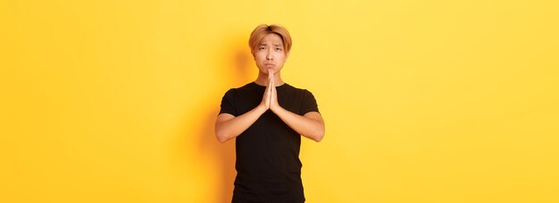 Портрет несчастного азиатского парня, умоляющего о помощи, стоящего на желтом фоне