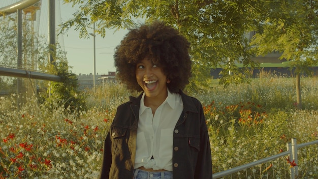 Free photo portrait of mixed race black woman in the park full of flowers laughing in contour sunlight laughing and making faces cinema film colors