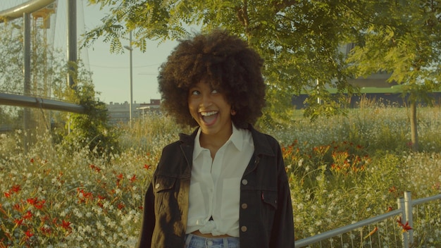 花でいっぱいの公園で混血の黒人女性の肖像画輪郭の日光で笑って笑って顔を作るシネマ映画の色