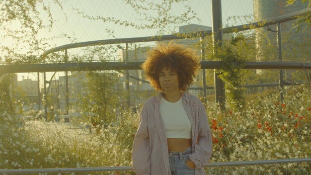 Portrait of mixed race black woman in the park full of flowers with huge afro hair in contour sunlight watching to the camera Cinema film colors