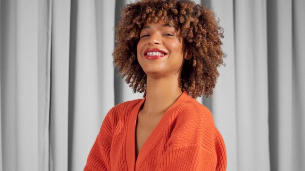 Portrait of mixed race black woman with textured curly afro hair in bright orange jacket with natural makeup for dark skin tones Smiling wide