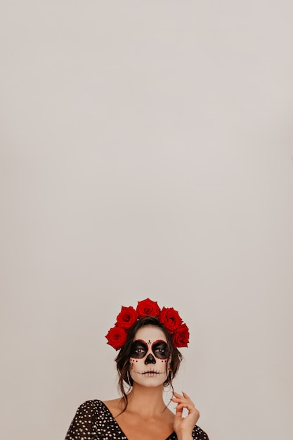 Portrait of model against white wall, posing in crown of natural flowers. halloween skeleton makeup looks unusual