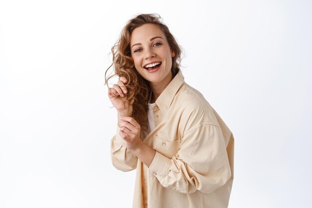 Portrait of modern blond woman touching curly blond hair, smiling and laughing happily, epxress positive emotions, standing over white background