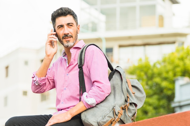 Portrait of a modern man in pink shirt carrying his backpack talking on mobile phone