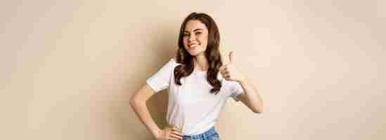 Free photo portrait of modern young woman showing thumbs up like and approve smiling pleased recommending compa
