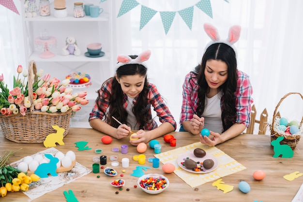 Portrait of mother and her daughter painting the easter eggs with brush on table