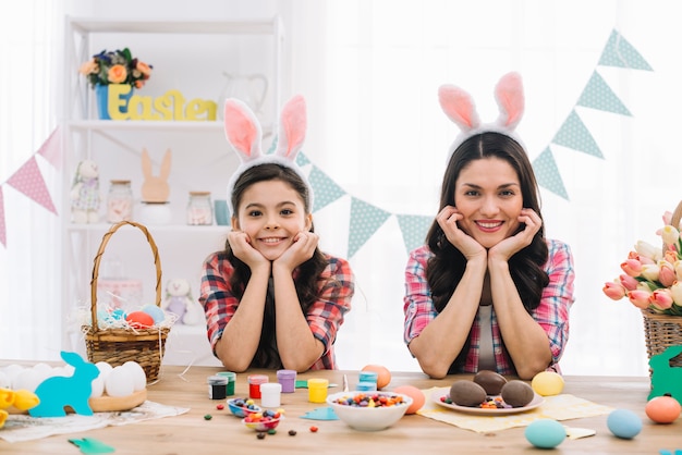 Портрет матери и ее дочери в ушах пасхального кролика, опираясь на стол с пасхальными конфетами