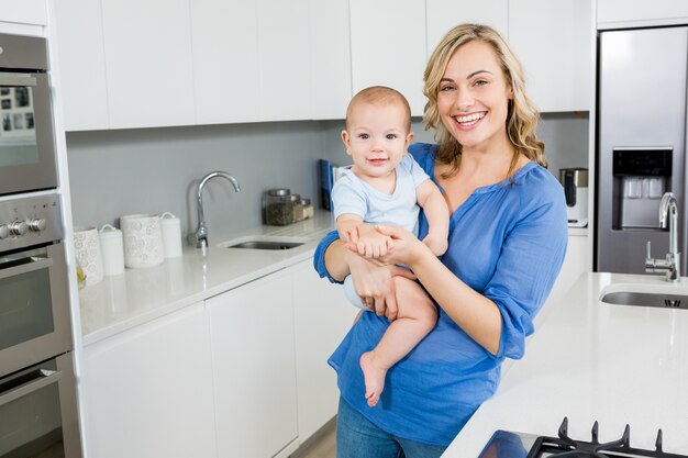 Portrait of mother holding her baby boy in kitchen