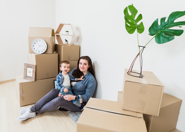 Portrait of mother sitting with her baby boy among the cardboard boxes in new home