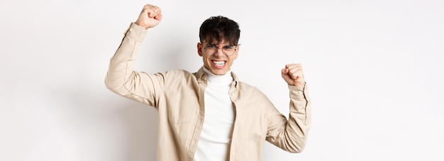 Free photo portrait of motivated young man feeling joy raising hands up and celebrating victory triumphing and