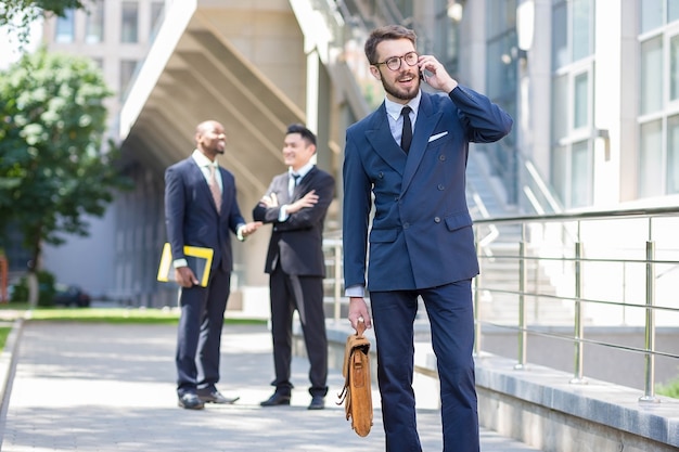 Portrait of multi ethnic business team.Three men standing against the background of city. The foreground of a European man  talking on the phone. Other men is Chinese and African-American.