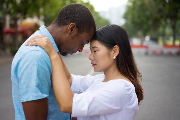 Portrait of multiethnic couple embracing and touching heads outdoors.