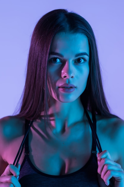 Portrait of muscular woman holding jumping rope, skipping rope on purple light