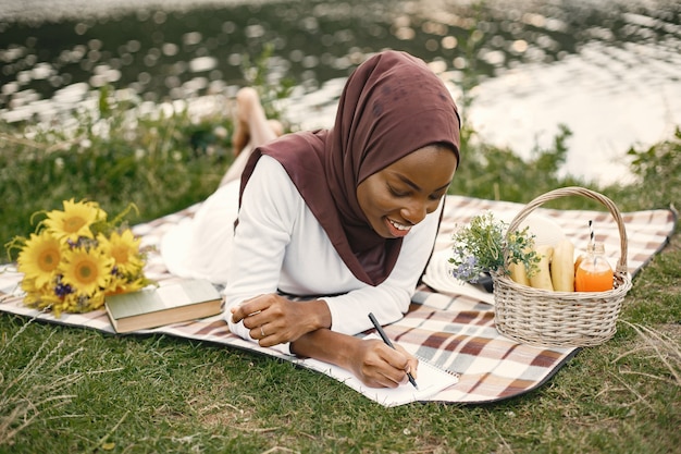 Free photo portrait of a muslim woman lay on the plaid picnic blanket near the river