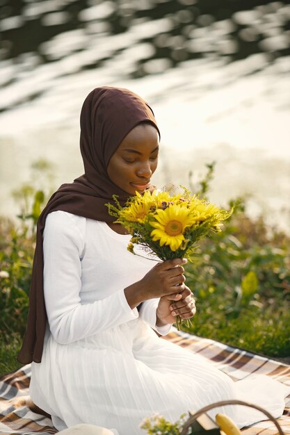 Portrait of a muslim woman sits on the plaid picnic blanket near the river