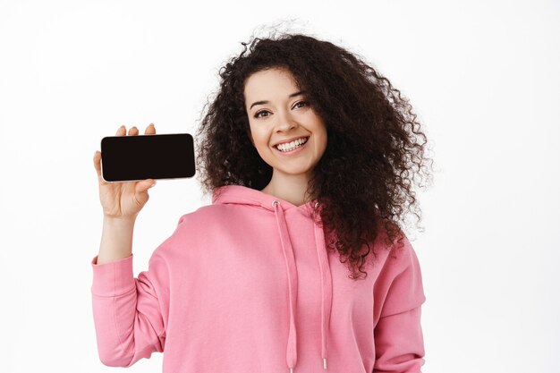 スマートフォンを保持している自然な笑顔の巻き毛の女性の肖像画
