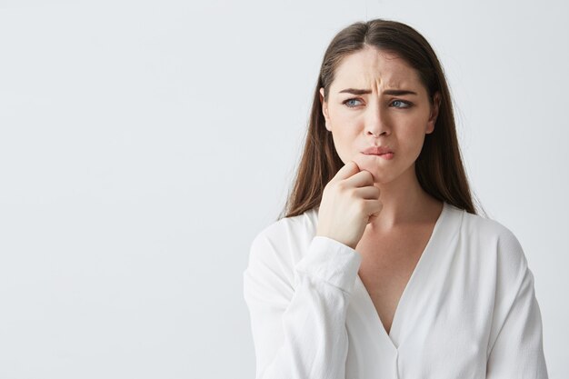 Portrait of nervous young brunette girl thinking looking in side holding hand on chin .