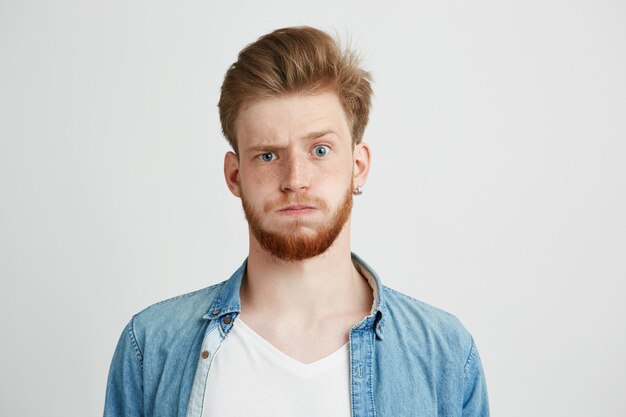 Portrait of nervous young man with beard raising up brow.