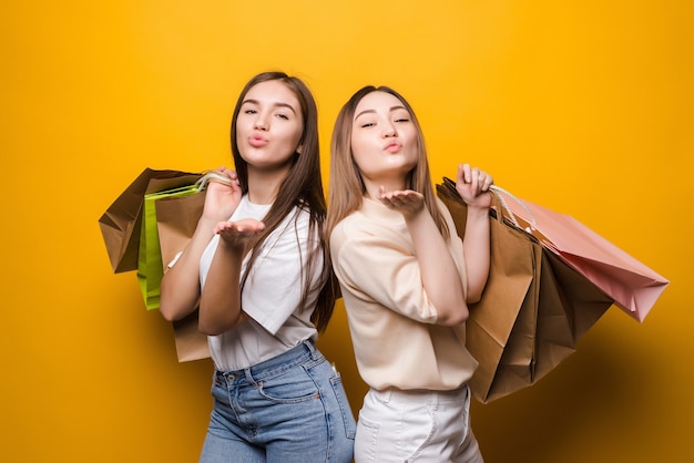 Free photo portrait of nice attractive girls carrying colorful bags sending air kiss having fun isolated on bright vivid shine vibrant yellow color wall