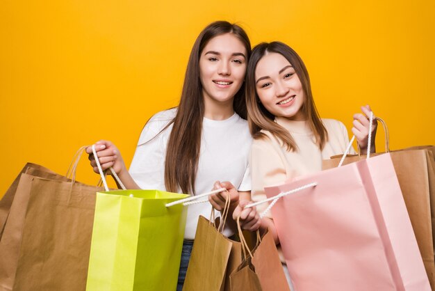 Portrait of nice attractive pretty girls carrying colorful bags having fun isolated on yellow color wall