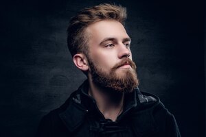 portrait of a bearded urban male isolated with contrast illumination on grey vignette background.