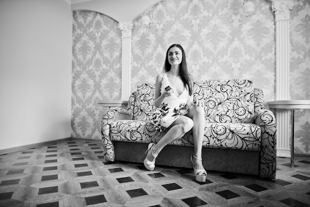 彼女の手でリモコンでソファに座っている花柄のドレスを着た美しい少女の肖像画白黒写真