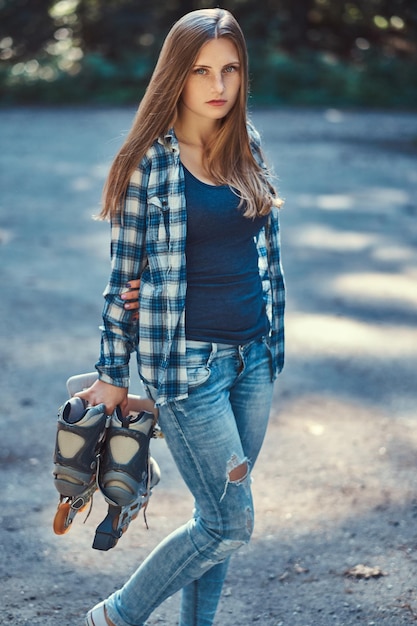 フリースのシャツとジーンズを身に着けている長い髪の美しい少女の肖像画は、田舎に立って、ローラーを保持しています。