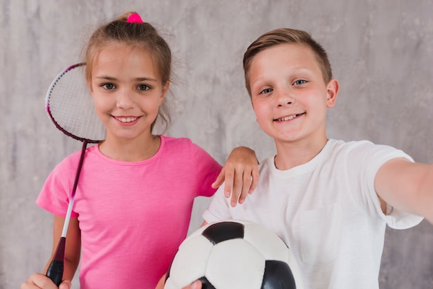Портрет мальчика и девочки игроков с ракеткой и футбольным мячом перед бетонной стеной