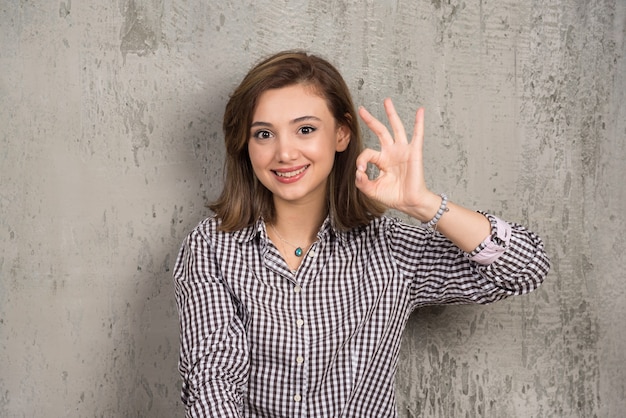 Бесплатное фото Портрет милой молодой женщины, показывающей пальцами знак ок и смотрящей вперед