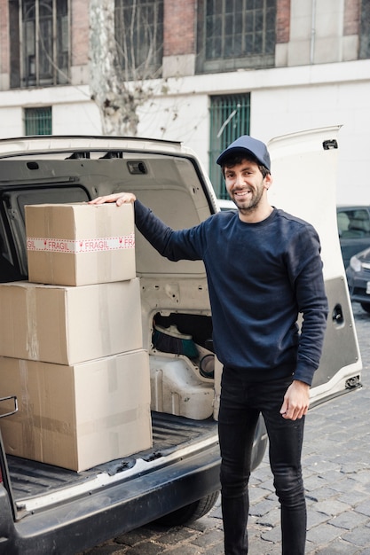 Бесплатное фото Портрет счастливой доставки человек стоял возле автомобиля с картонные коробки