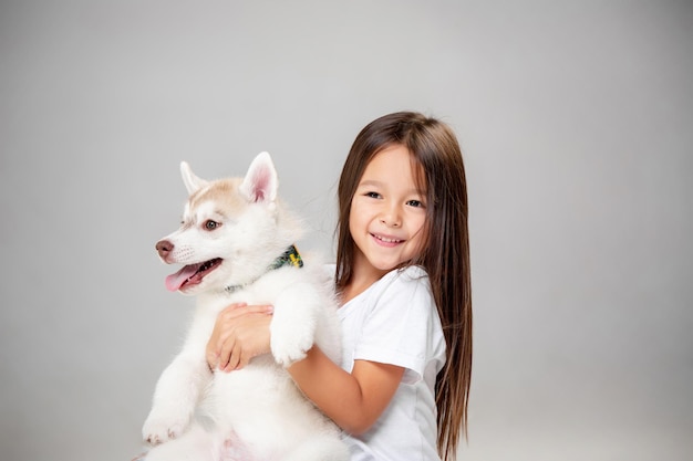 Портрет радостной маленькой девочки, весело проводящей время с щенком сибирской хаски на полу в студии. животное, дружба, любовь, домашнее животное, детство, счастье, собака, концепция образа жизни
