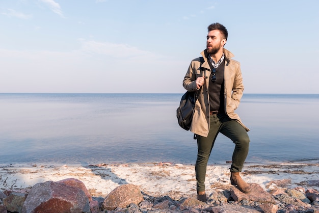 Бесплатное фото Портрет мужчины турист с сумочкой на плече, стоя перед морем