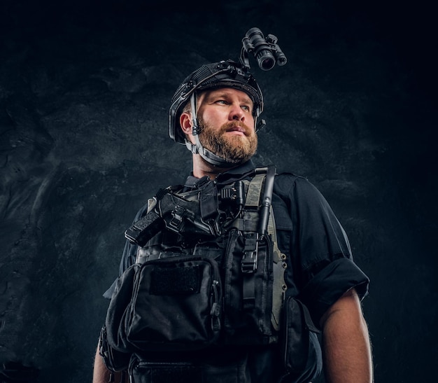 야간 투시경이 있는 방탄복과 헬멧을 쓴 특수 부대 군인의 초상화. 어두운 질감의 벽에 대한 스튜디오 사진