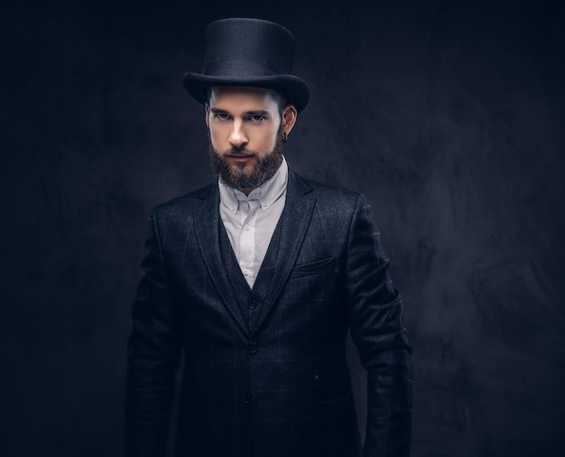 Бесплатное фото Портрет стильного бородатого мужчины в элегантном костюме и цилиндрической шляпе, смотрящего в камеру на темном фоне.