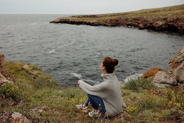 회색 스웨터를 입은 여성의 초상화는 변하지 않은 바위 해안 자연 위에 서 있다