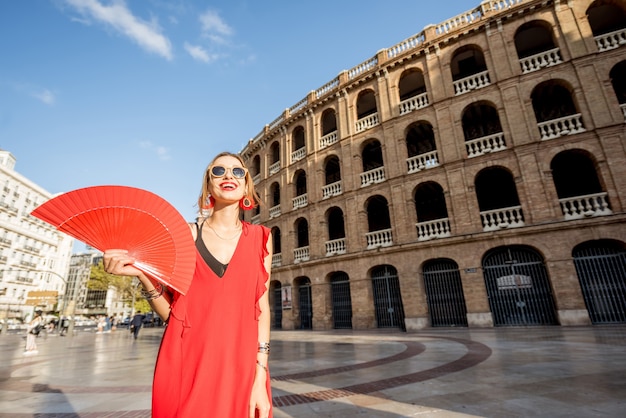 Портрет женщины в красном платье с испанским веером перед амфитеатром арены в валенсии, испания