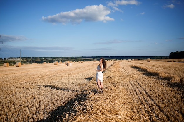 밀밭에 있는 젊은 곱슬머리 여성의 초상화. 밀이 깎이고 다발이 서서 자연을 즐기고 있습니다. 자연. 태양 광선 농업 프리미엄 사진