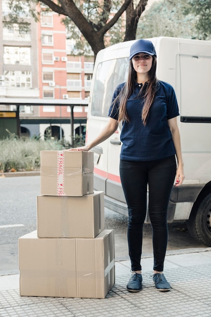Бесплатное фото Портрет молодой женщины курьерской стоять с уложенными картонные коробки