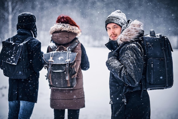 無料写真 冬の森の中を彼の友人と歩いているバックパックを持つ若いハイカーの男の肖像画